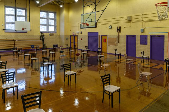 A school gymnasium, now converted to a temporary vaccination site, full of evenly spaced out seats.